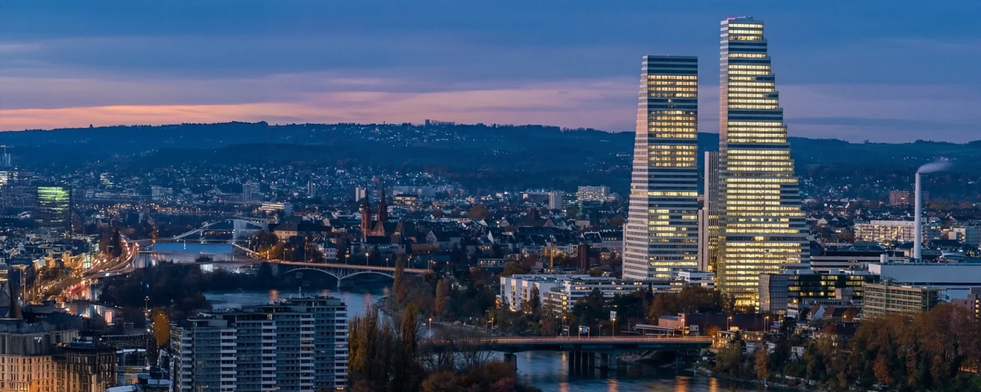 Abendliche Skyline von Basel mit beleuchteten Hochhäusern und Stadtansicht.