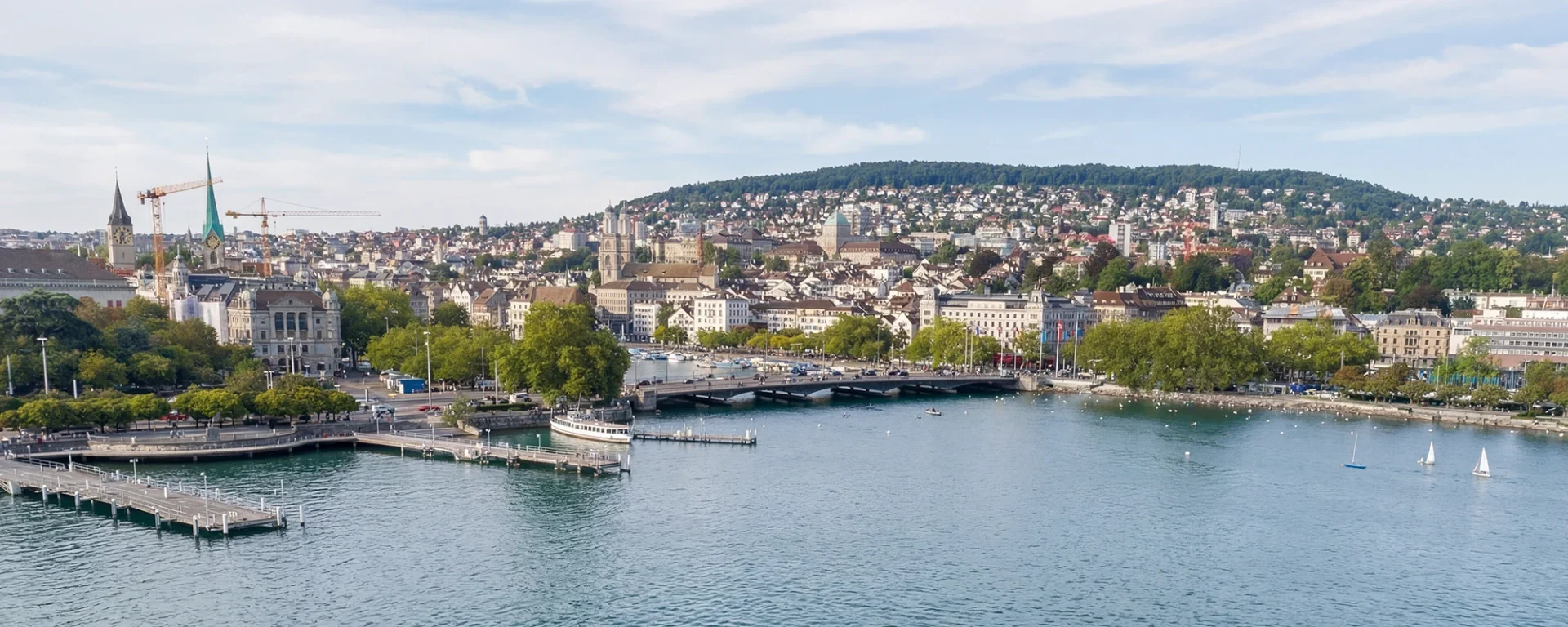 Panorama von Zürich mit See, Altstadt und grünen Hügeln im Hintergrund bei klarem Himmel.
