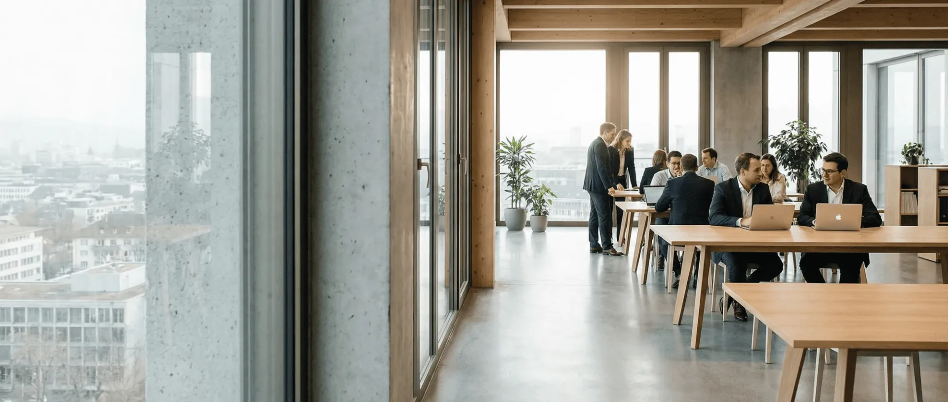 Modernes Büro mit großen Fenstern, wo Teams an hölzernen Schreibtischen in einer offenen, hellen Umgebung arbeiten.